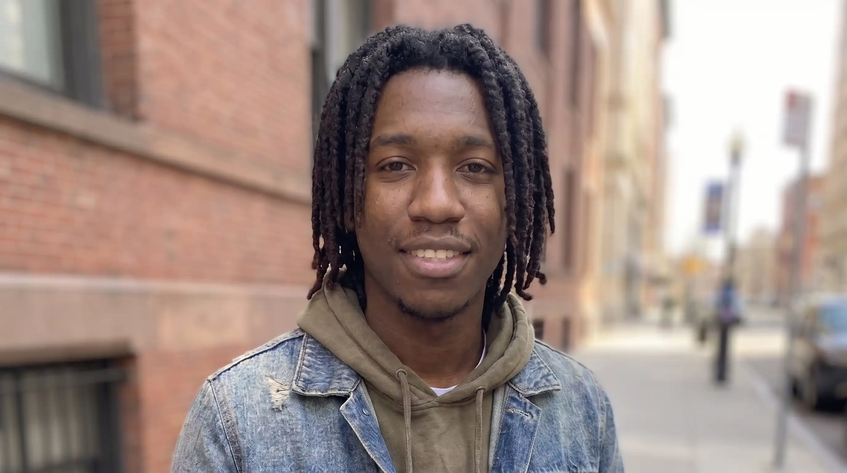 Replacement character — young Black man with locs in denim jacket on city street